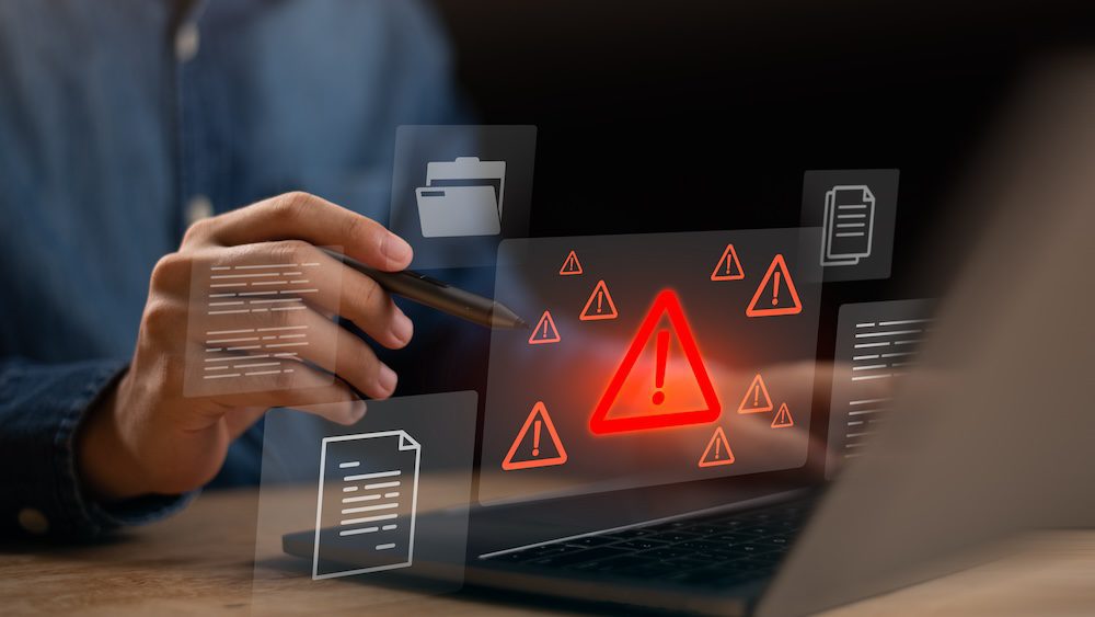 A person using a laptop is surrounded by digital warning icons and document symbols, highlighting an AI in managed services cybersecurity or data breach alert on the screen.